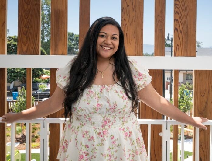 Woman with long dark hair stands smiling on an upstairs balcony of Colibri Commons in East Palo Alto.